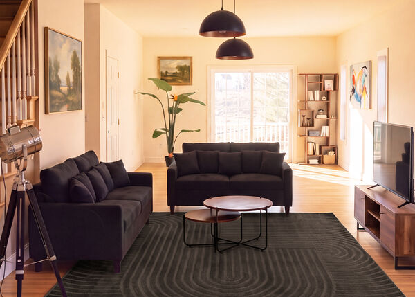 Modernes Wohnzimmer mit zwei dunklen Sofas, Satztischen, einem TV-M&ouml;bel und gro&szlig;em Teppich in einem hellen Raum.