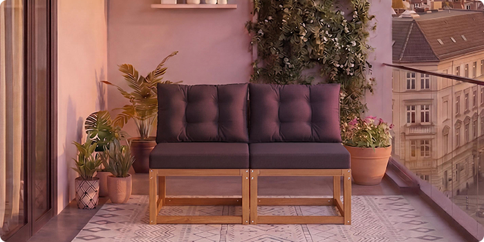 Zweiteiliges modulares Holzsofa mit dunkelgrauen Kissen auf einem Balkon mit Topfpflanzen und Stadtblick im Hintergrund